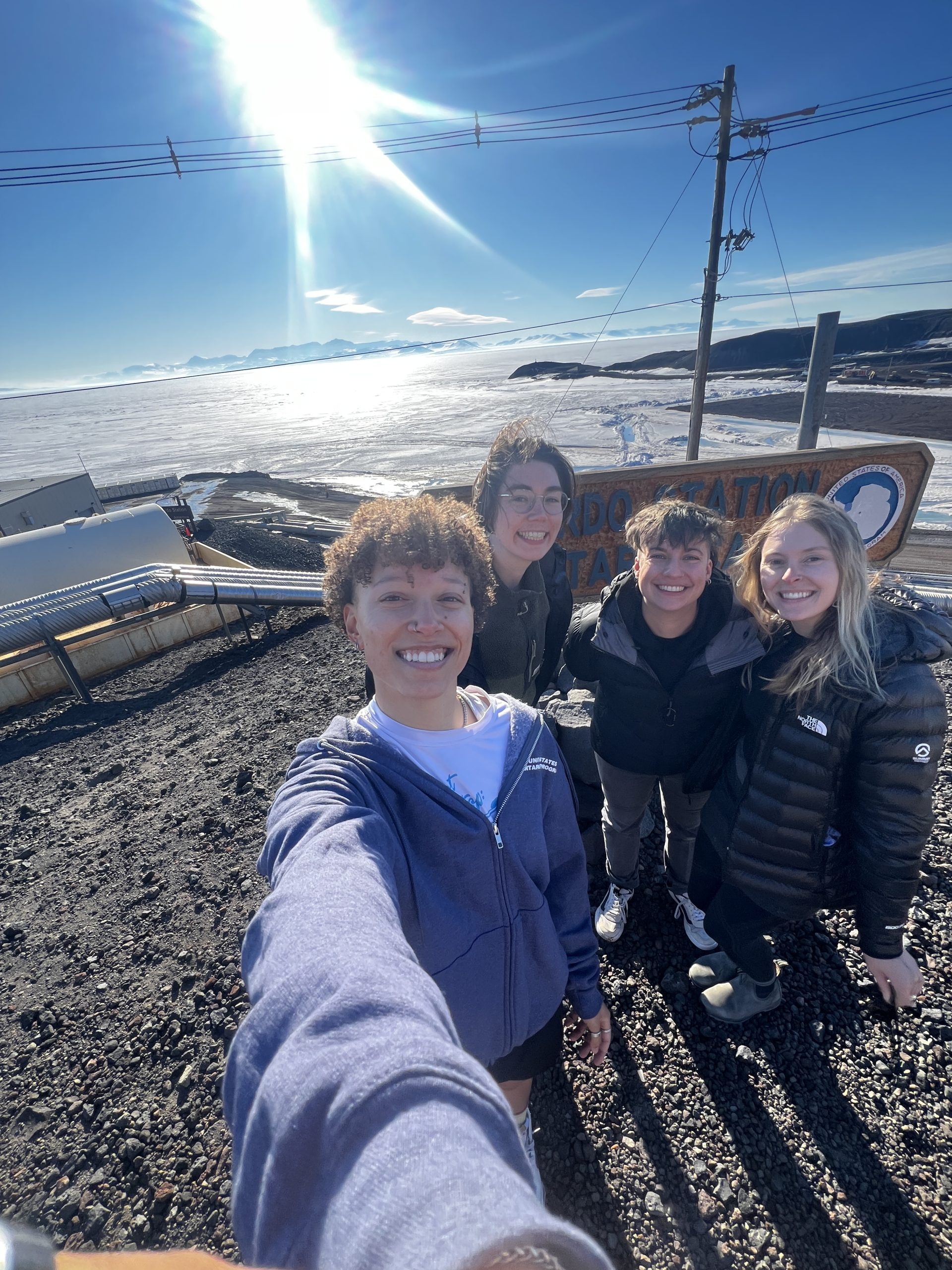 The remaining Taylor Dome team in front of the McMurdo sign and the midnight sun